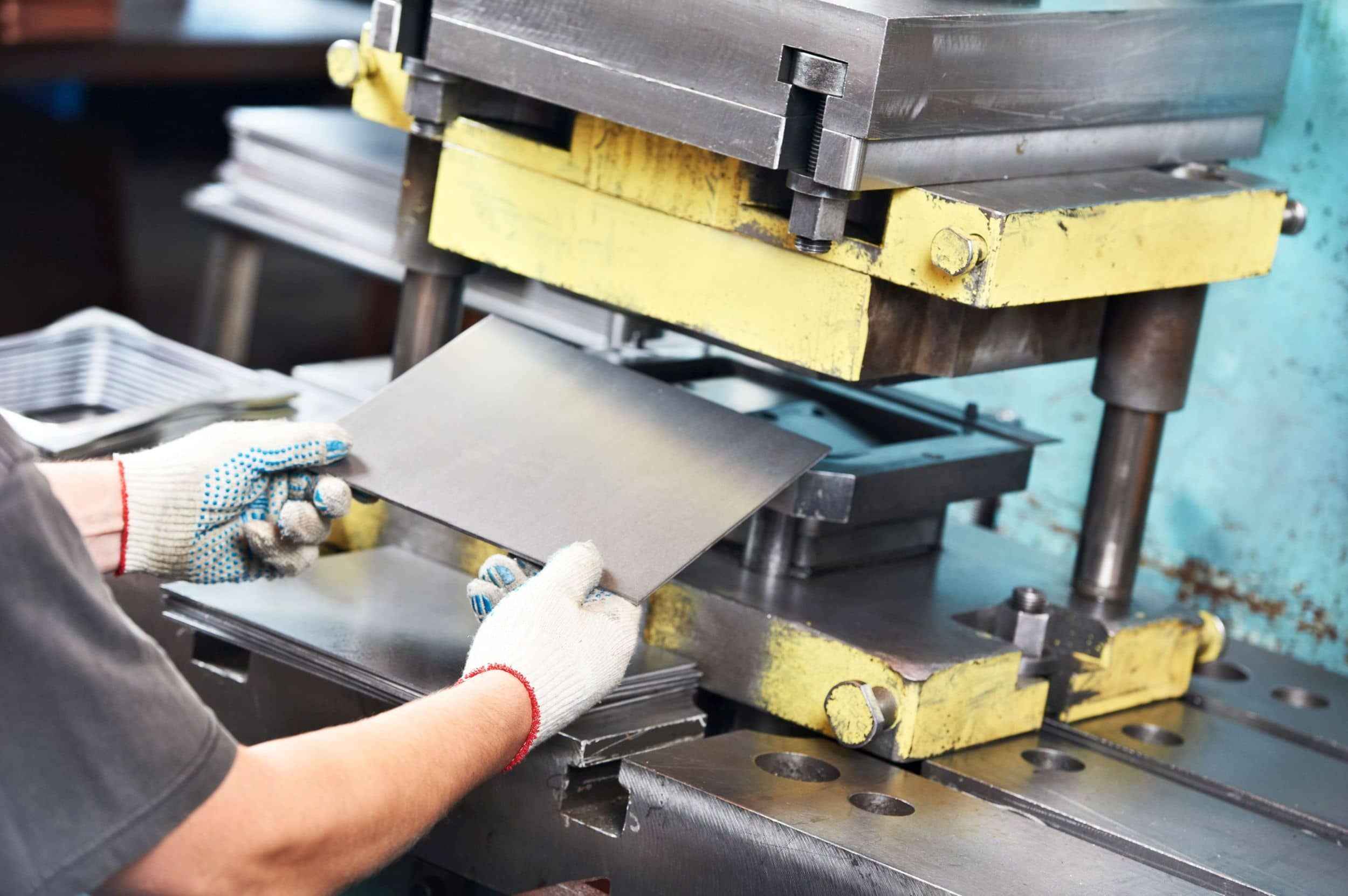 Fokusbranche Maschinenbau und Metallverarbeitung, Haftpflicht-Baustein: Ein Mitarbeitender schiebt eine Metallplatte in eine Stanzmaschine
