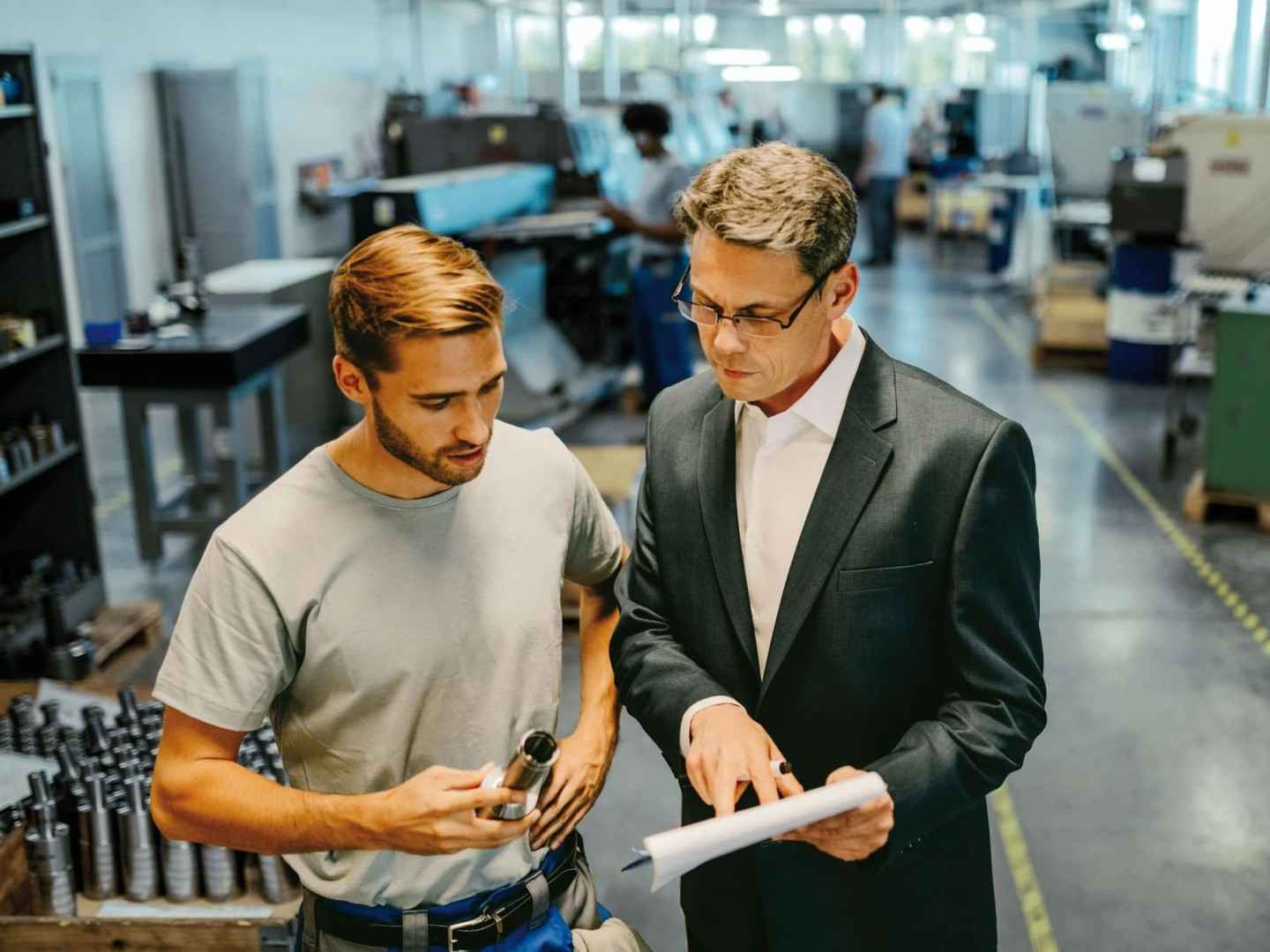Key-Visual Branchenkonzept Maschinenbau: Zwei Mitarbeitende besprechen einen Plan in einer Maschinenbauwerkstatt.