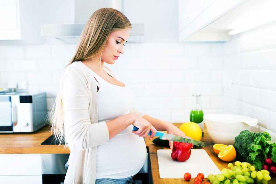 Baby-Care: Schwangere Frau schneidet Gemüse
