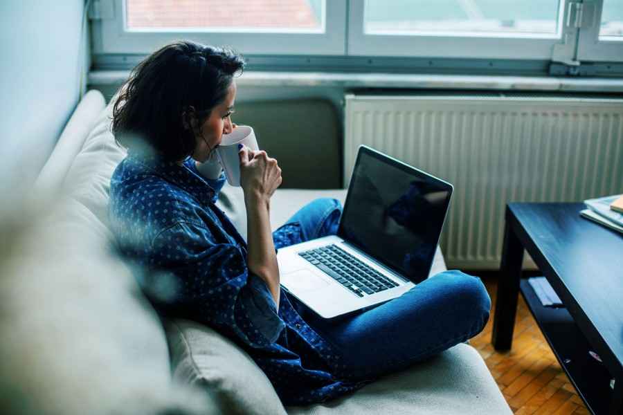 Frau mit Laptop auf Sofa trinkt Tee
