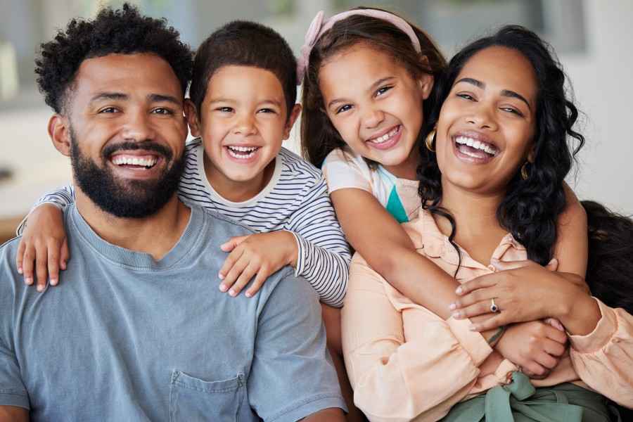 Eiin Paar mit Ihren zwei Kindern sitzen auf der Couch und lächeln.