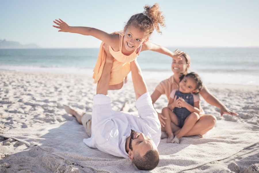 Familie am Strand, der Vater lässt die Tochter in der Luft Flugzeug spielen