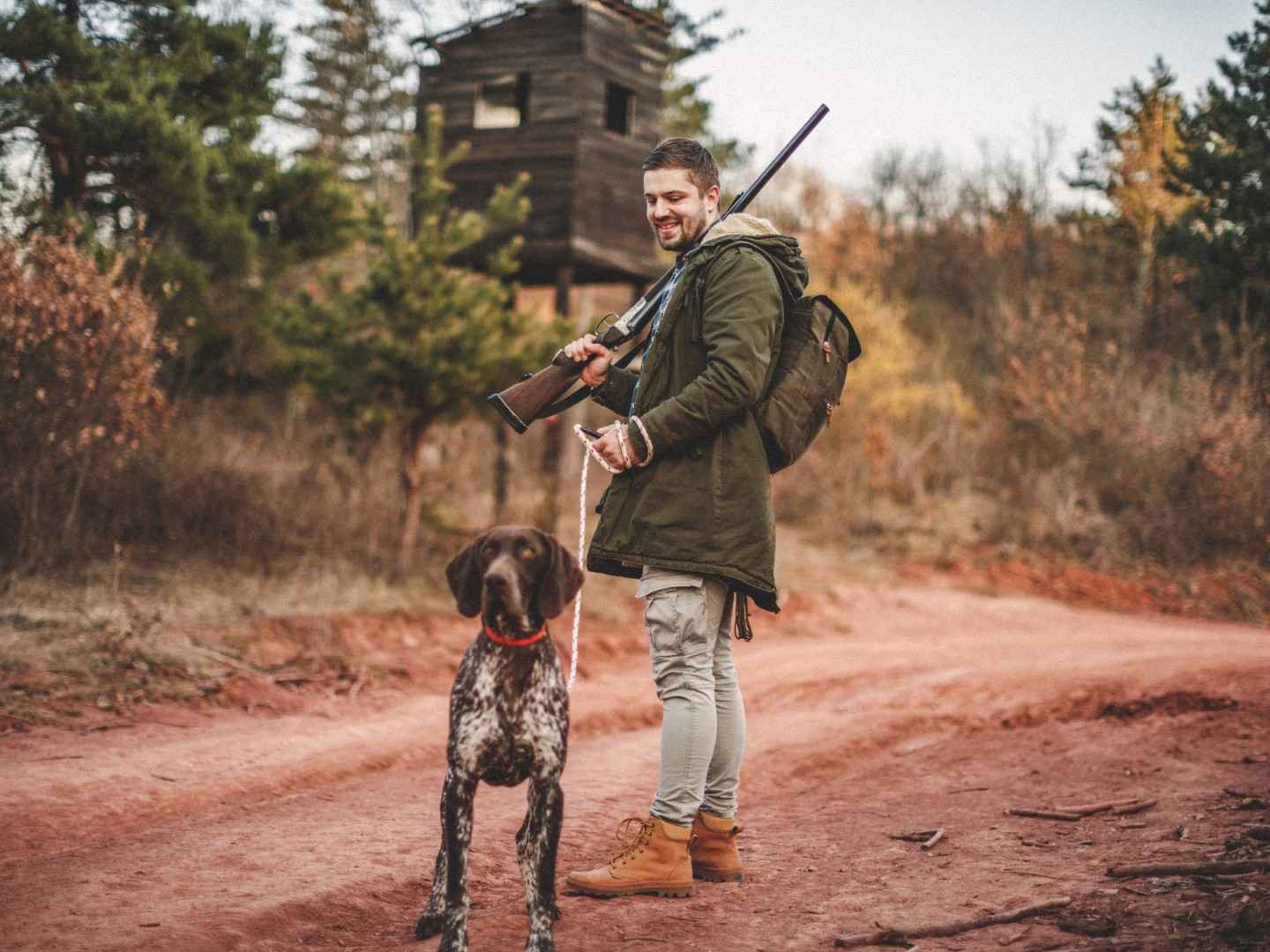 Ein Jäger steht mit seinem Jagdhund vor einem Hochsitz