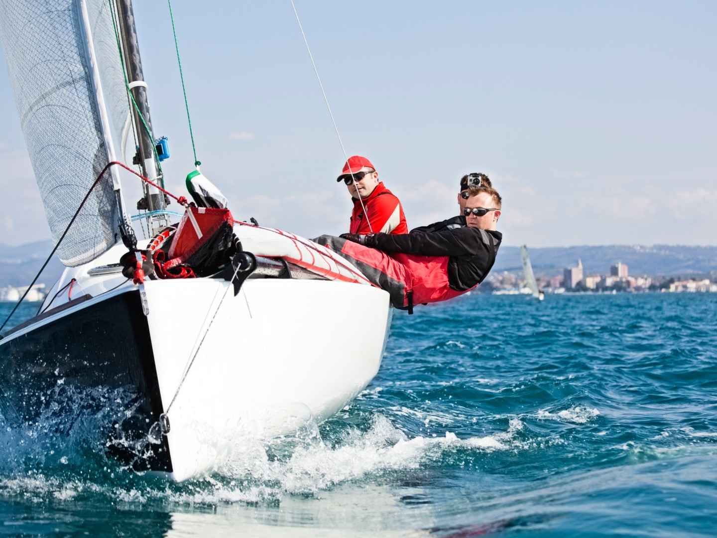 Junge Männer segeln und hängen sich dabei weit aus dem Boot