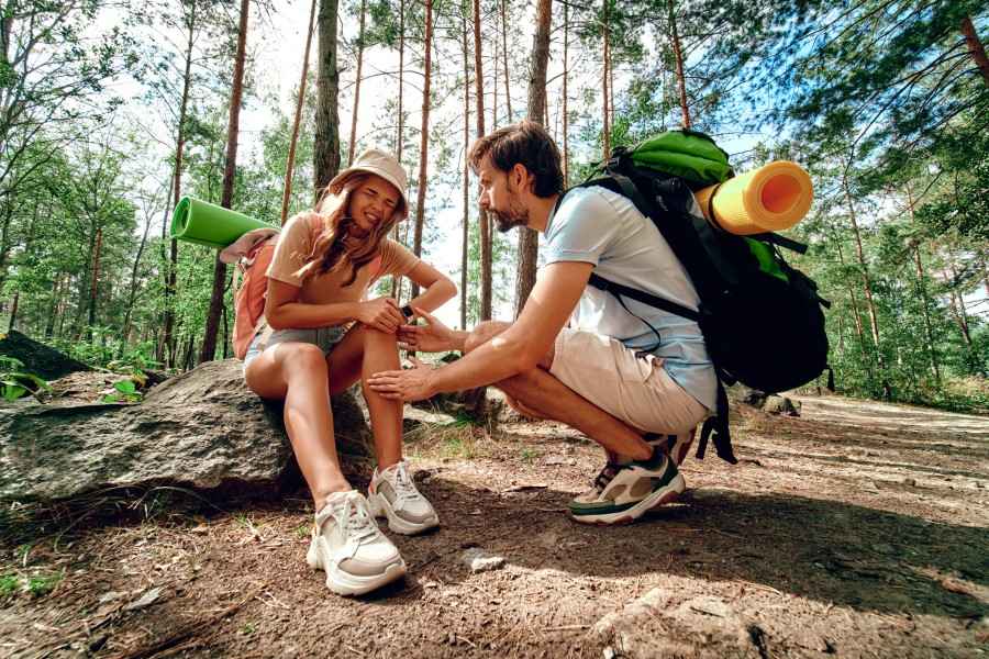 Eine Frau hat sich auf einer Wanderung verletzt und wird von ihrem Freund zu ihren Beschwerden befragt.