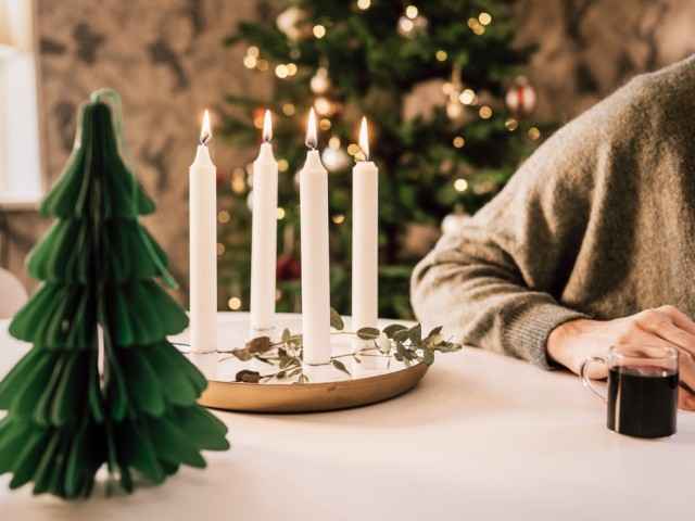Gothaer Ratgeber: Vier brennende Kerzen stehen auf dem Tisch. Im Hintergrund ist ein Weihnachtsbaum.