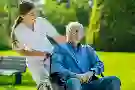 Eine Pflegerin schiebt einen älteren Patienten im Rollstuhl im Park spazieren. Eine Pflegerin schiebt einen älteren Patienten im Rollstuhl im Park spazieren.